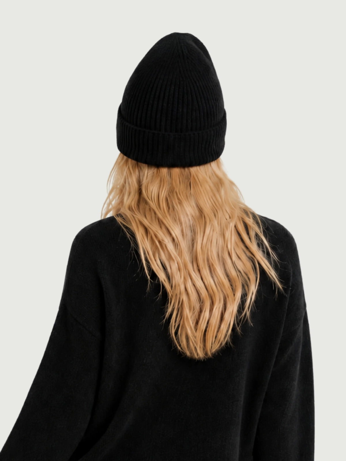 Vista posteriore modella indossa berretto beanie nero a coste verticali, risvolto alto e calotta arrotondata