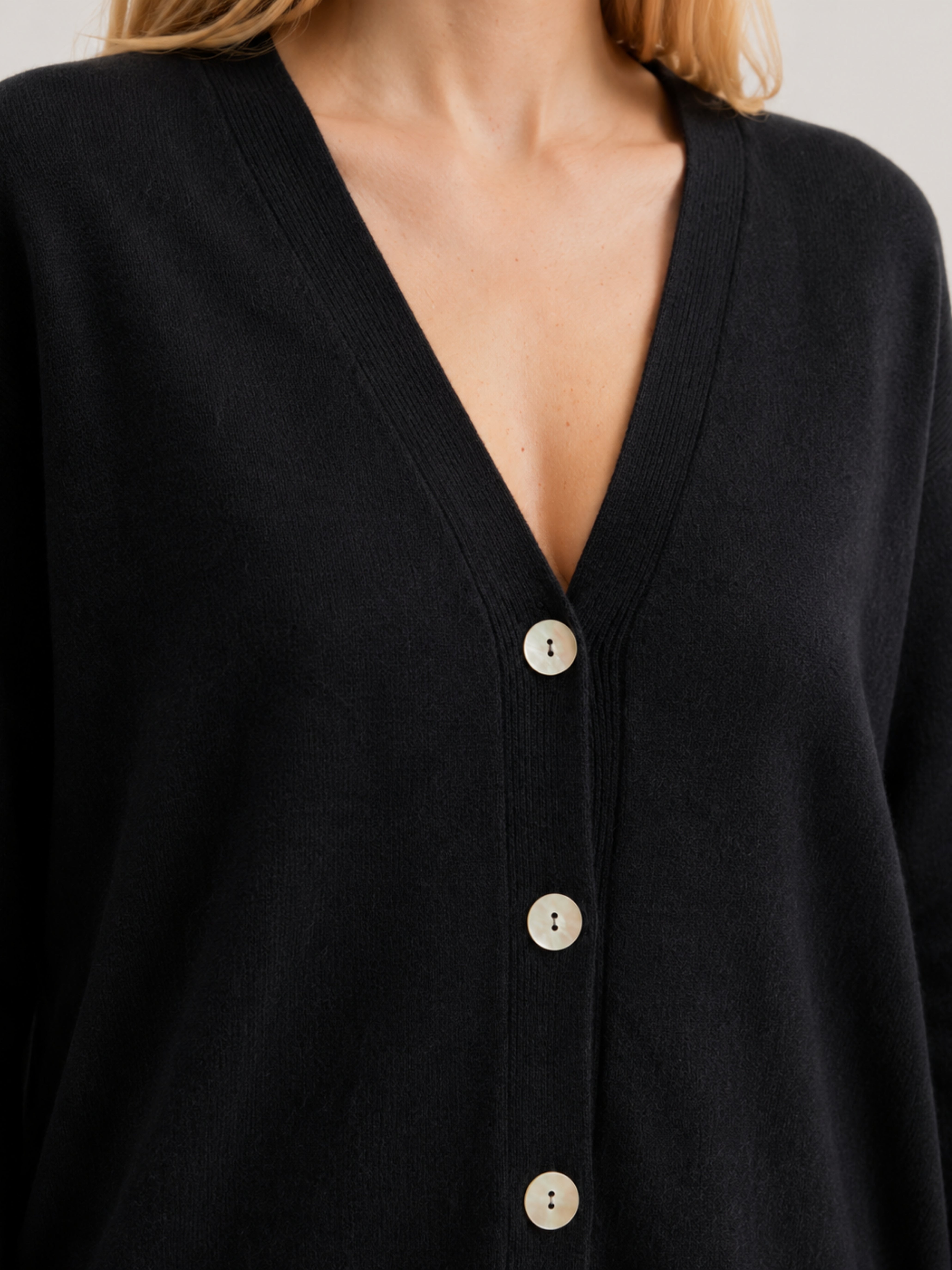 Dettaglio cardigan over nero, scollo a V, manica lunga con polsino a costine, chiusura con bottoni effetto madreperla