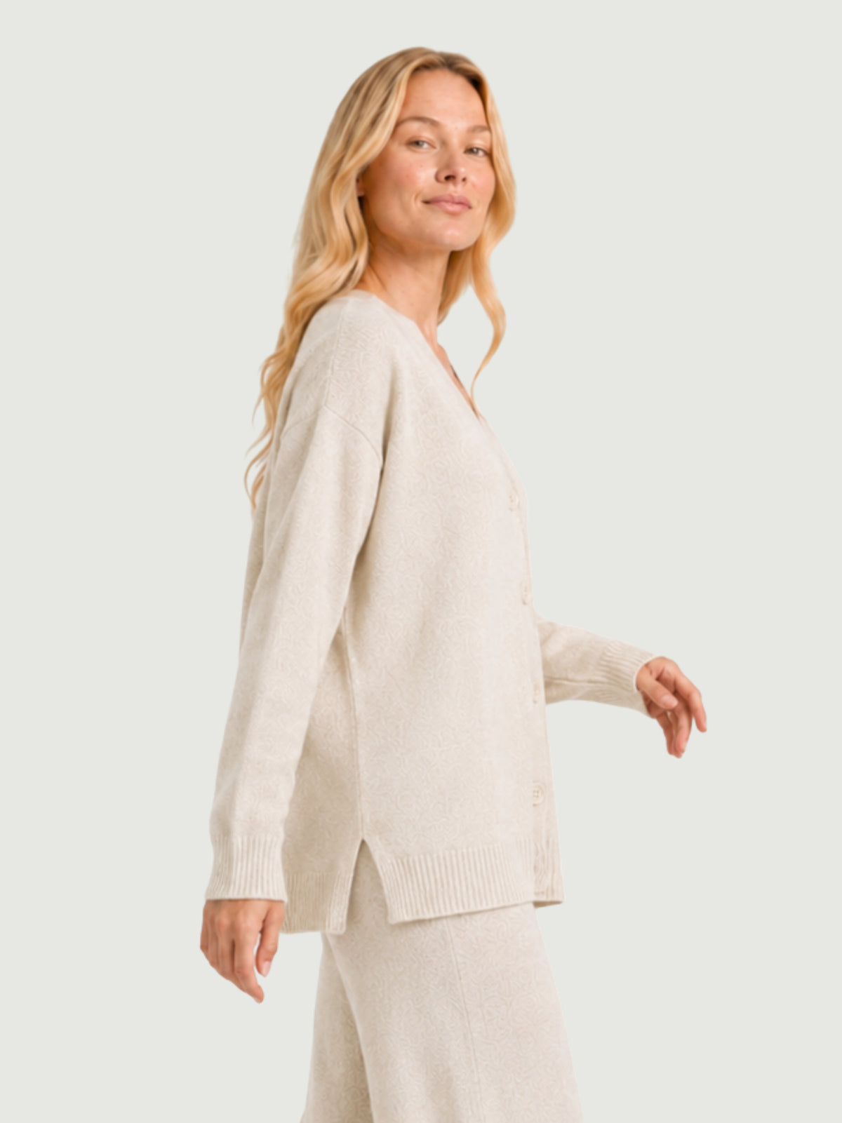 Vista laterale modella indossa cardigan over bianco panna, scollo a V, manica lunga con polsino a costine, chiusura con bottoni effetto madreperla