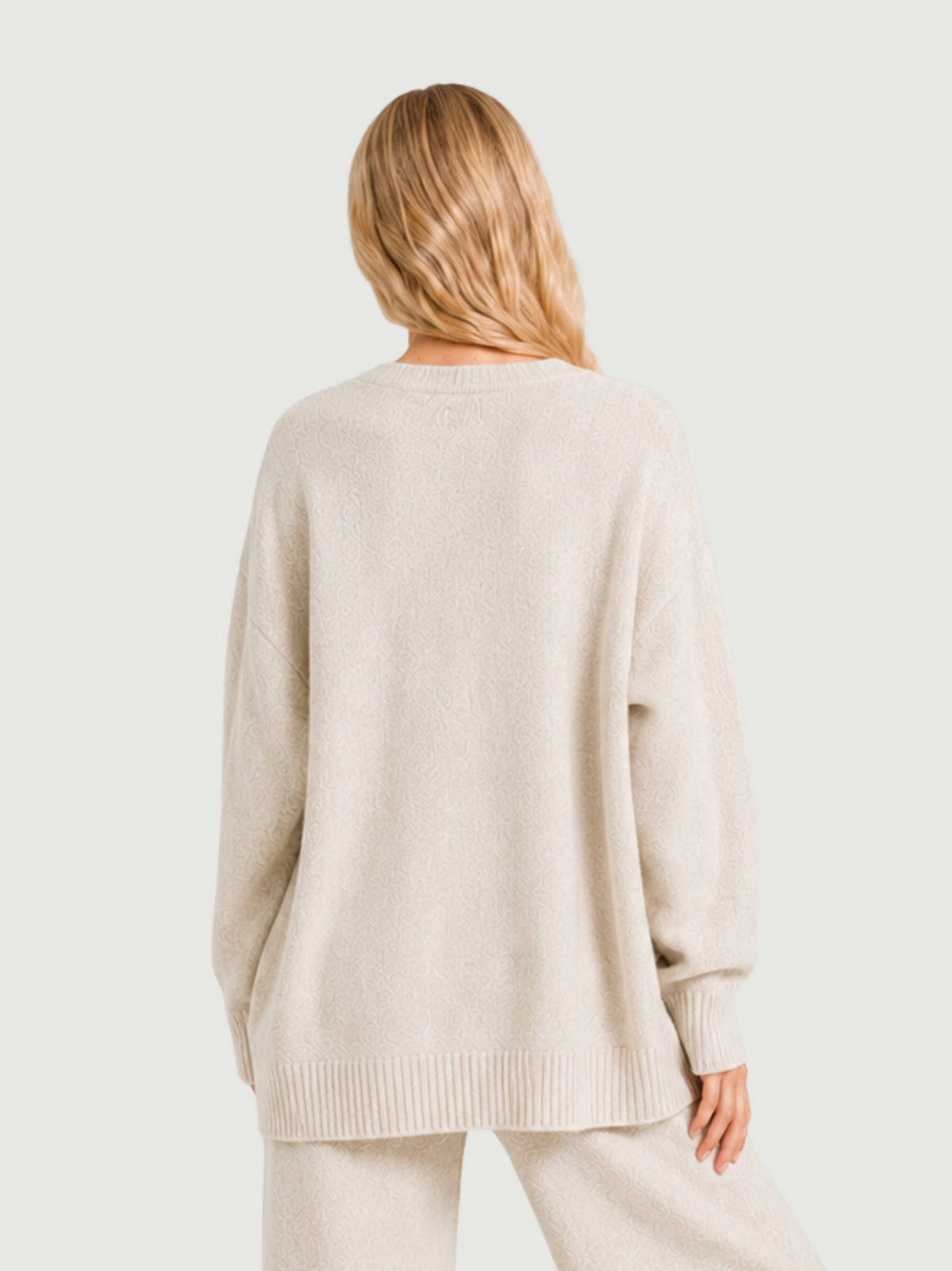 Vista posteriore modella indossa cardigan over bianco panna, scollo a V, manica lunga con polsino a costine, chiusura con bottoni effetto madreperla