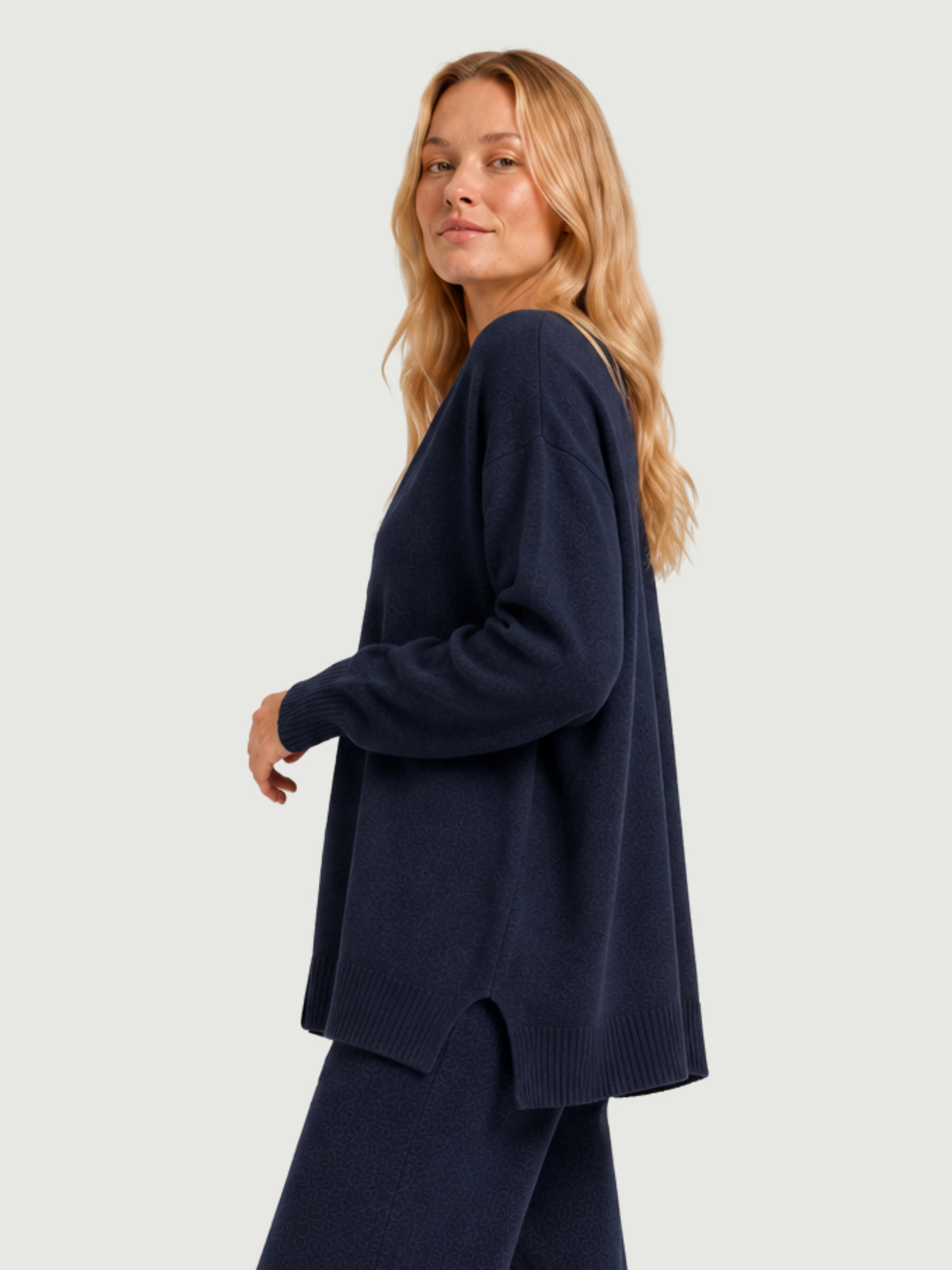 Vista laterale modella indossa cardigan over blu scuro, scollo a V, manica lunga con polsino a costine, chiusura con bottoni effetto madreperla