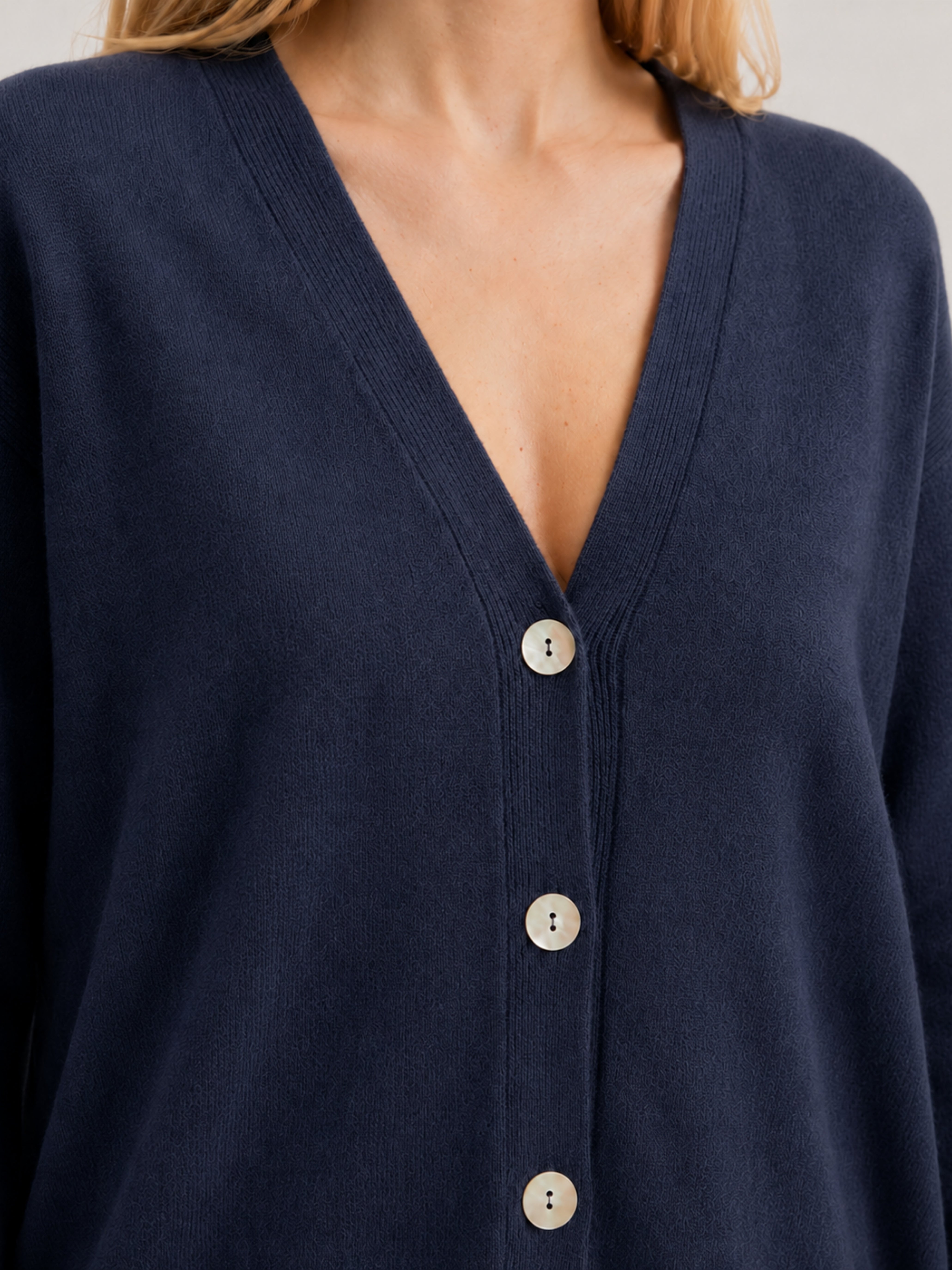 Dettaglio cardigan over blu scuro, scollo a V, manica lunga con polsino a costine, chiusura con bottoni effetto madreperla