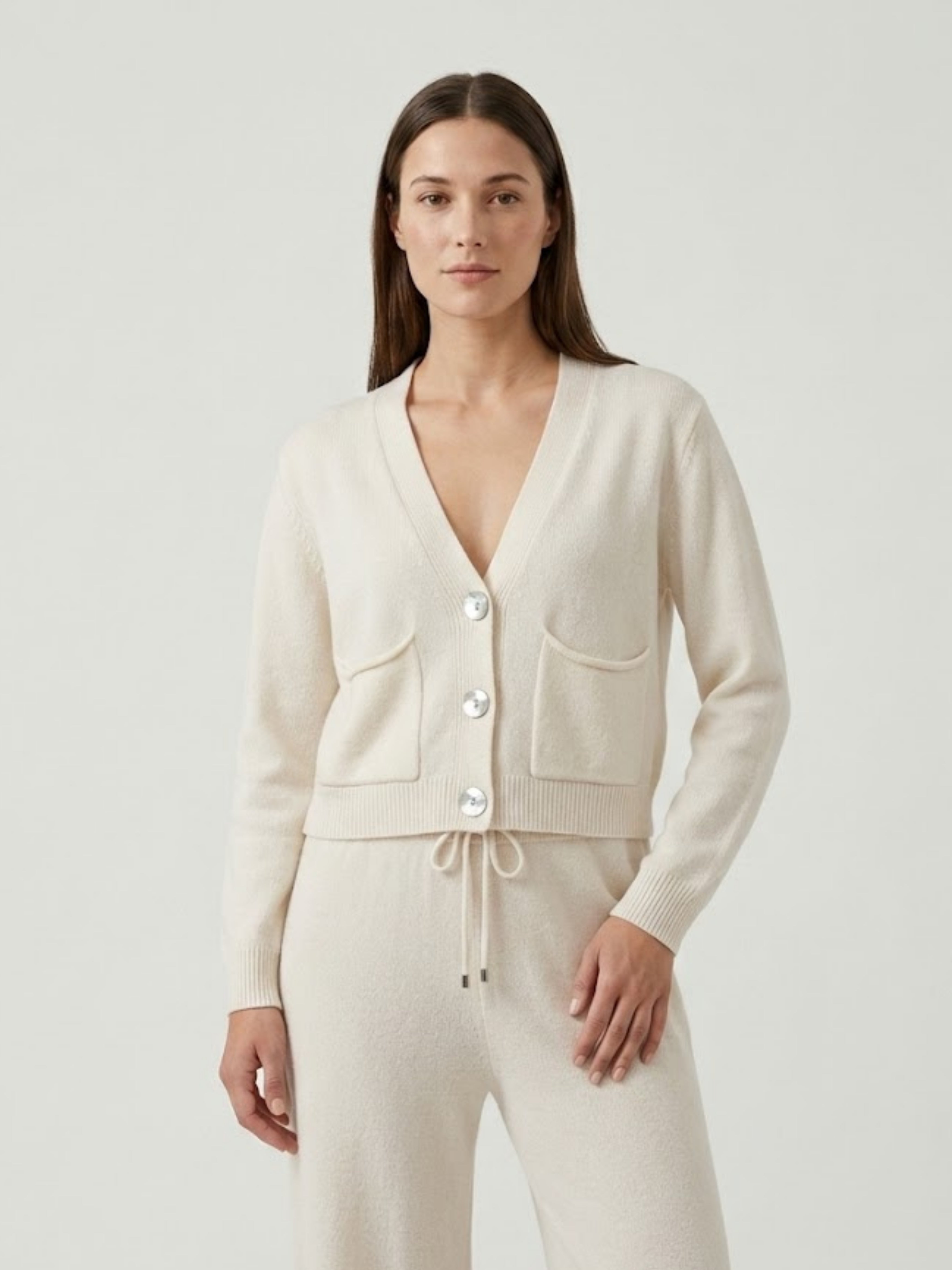Modella indossa cardigan cropped bianco panna con scollo a V, chiusura frontale con bottoni effetto madreperla, taschini applicati SOF - BiMOR