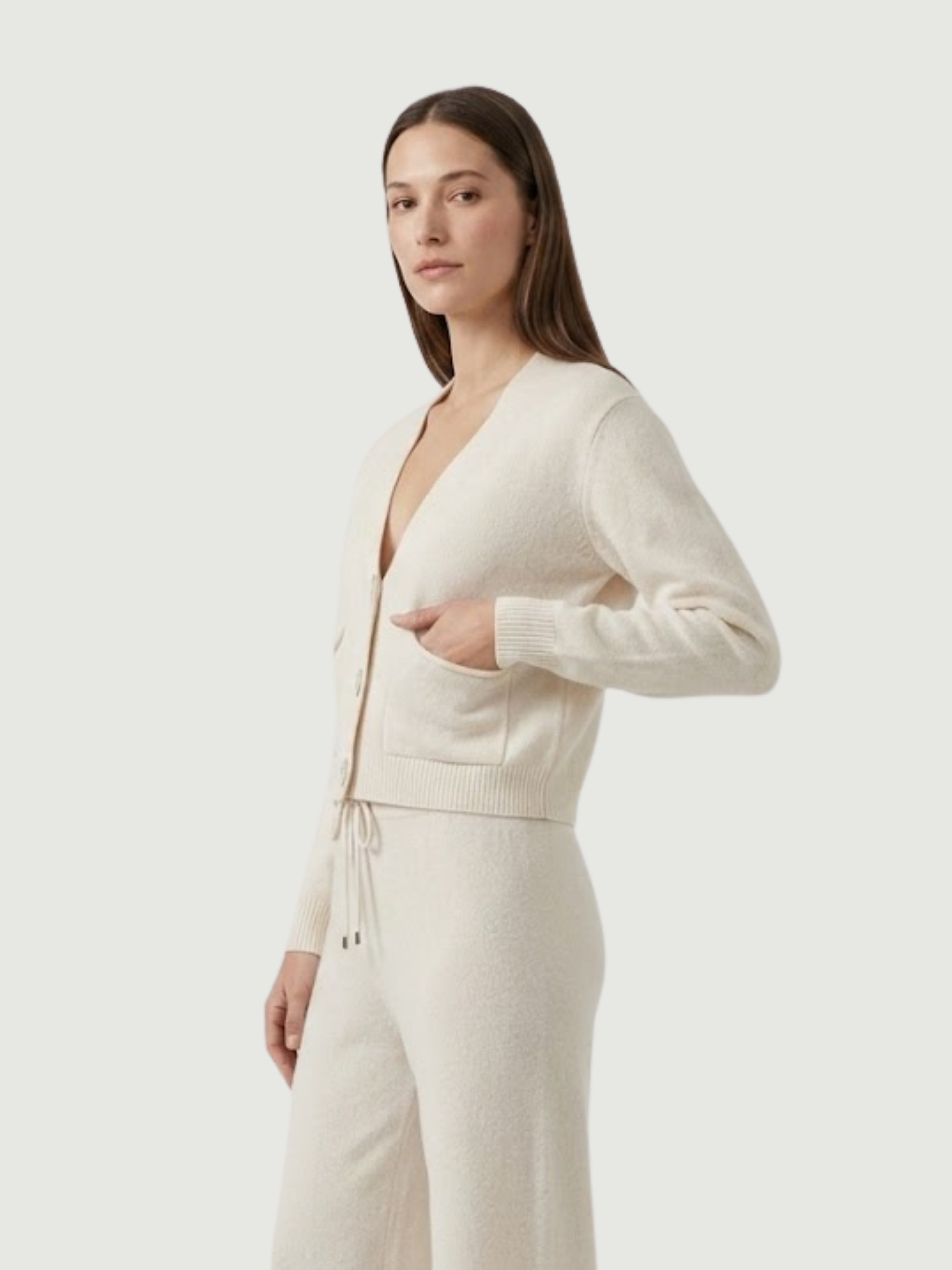Vista laterale modella indossa cardigan cropped bianco panna con scollo a V, chiusura frontale con bottoni effetto madreperla, taschini applicati