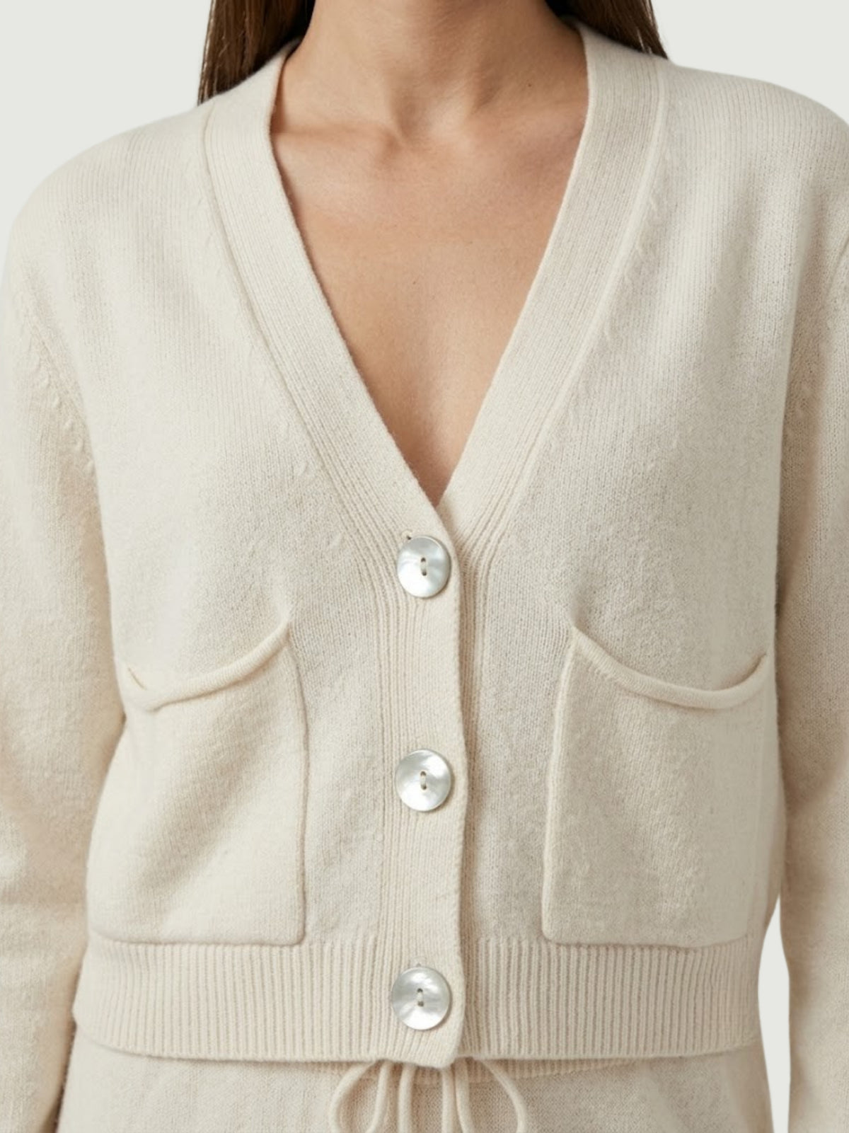 Dettaglio cardigan cropped bianco panna con scollo a V, chiusura frontale con bottoni effetto madreperla, taschini applicati