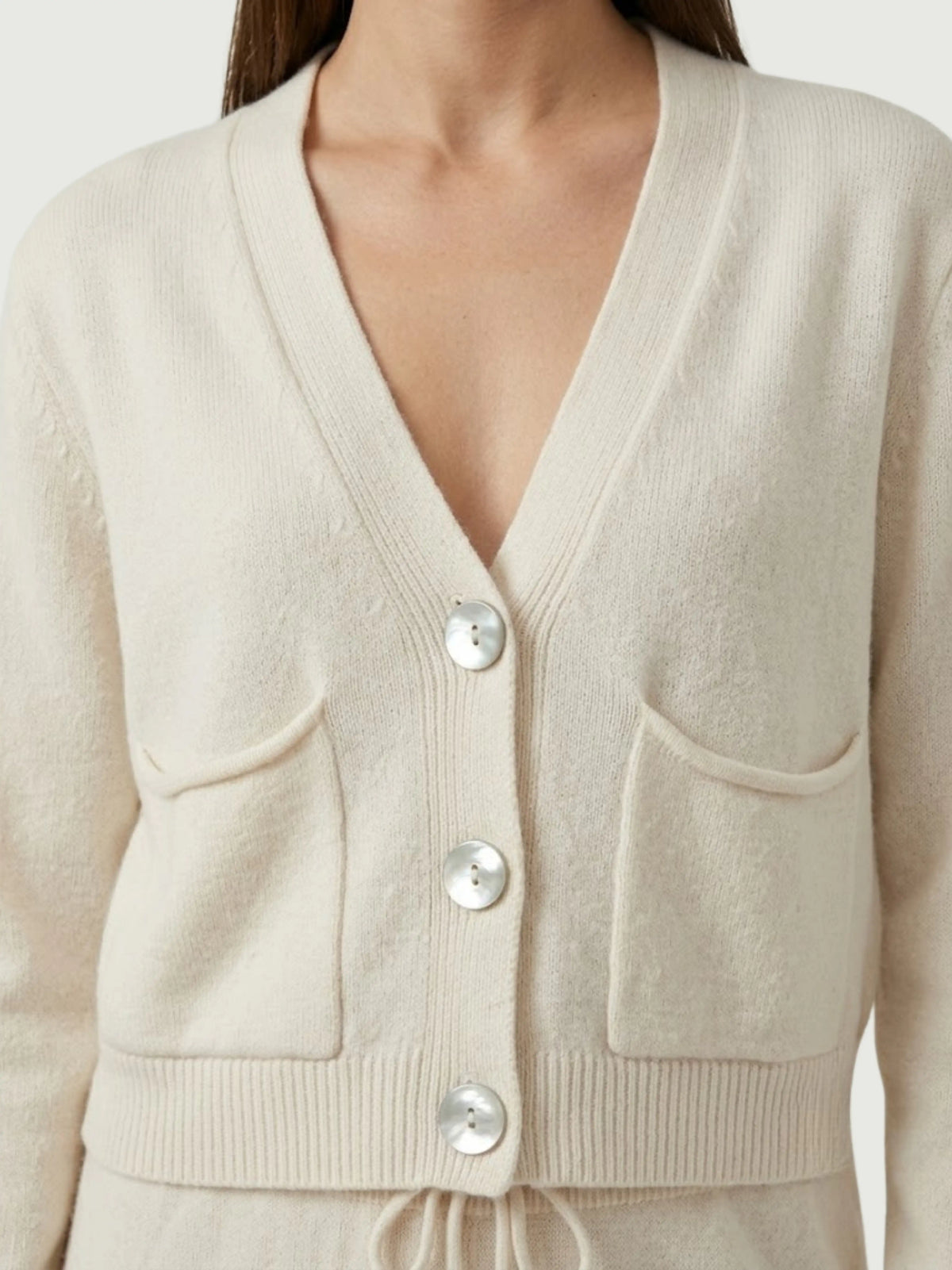 Dettaglio cardigan cropped bianco panna con scollo a V, chiusura frontale con bottoni effetto madreperla, taschini applicati