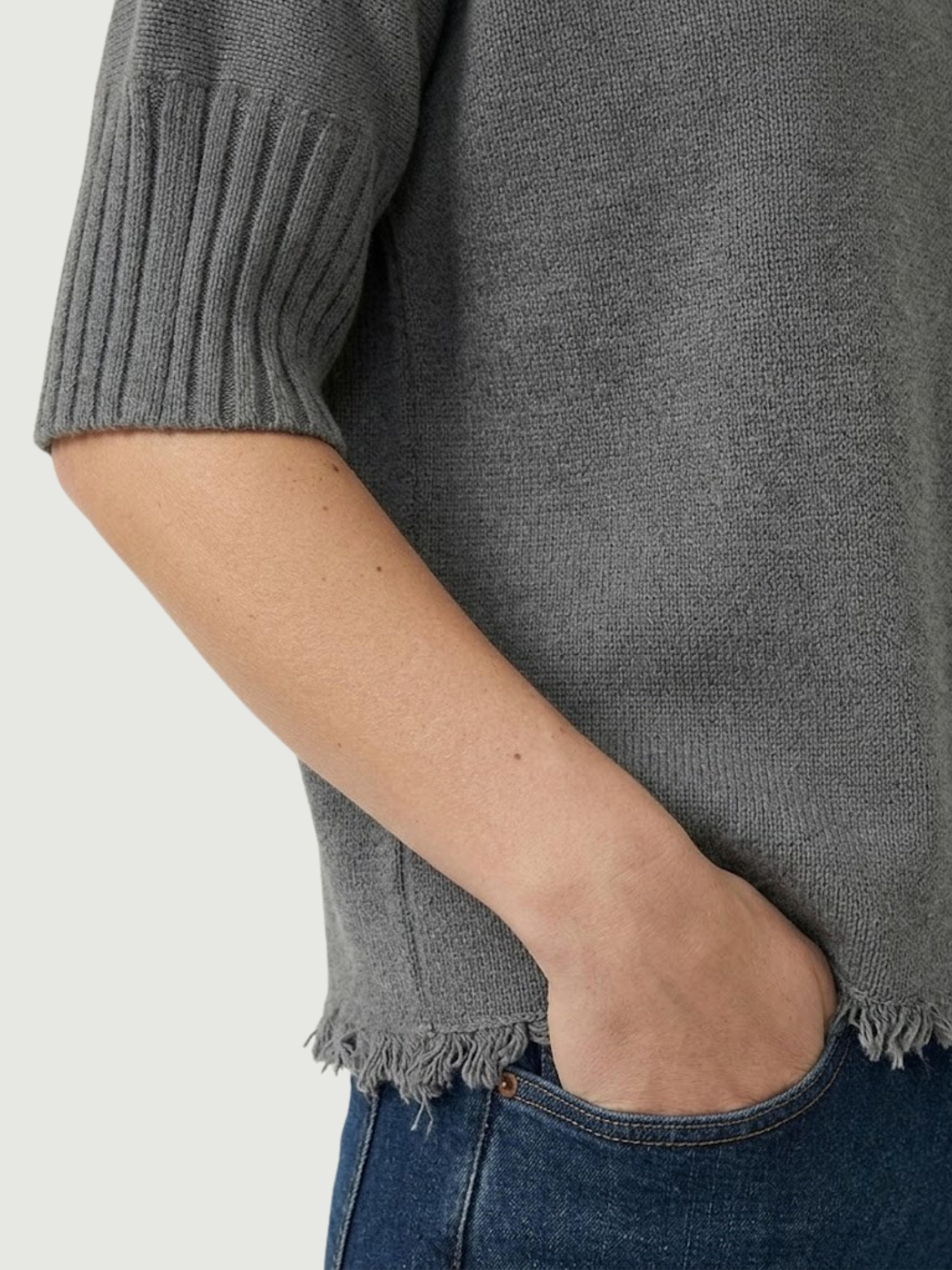 Dettaglio maglia lupetto grigia con manica a tre quarti e fondo sfrangiato