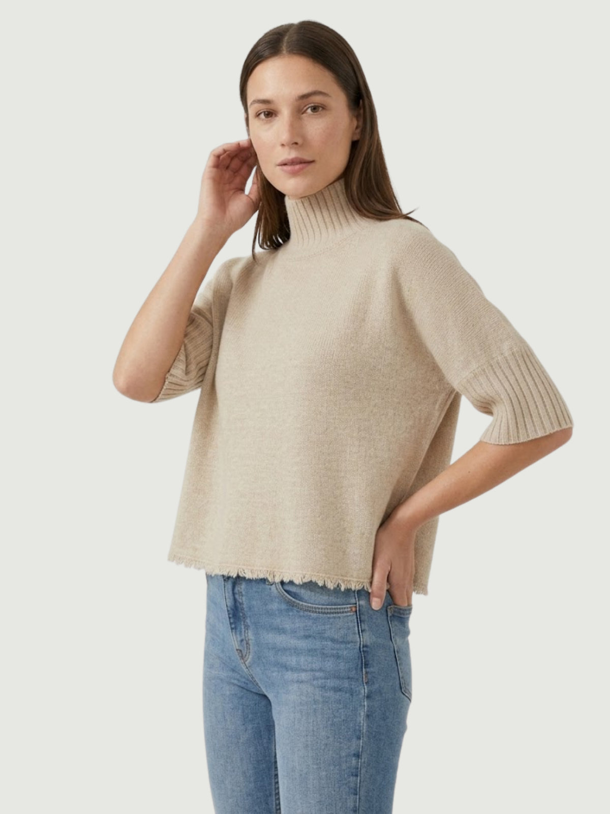 Vista laterale modella indossa maglia lupetto beige con manica a tre quarti e fondo sfrangiato