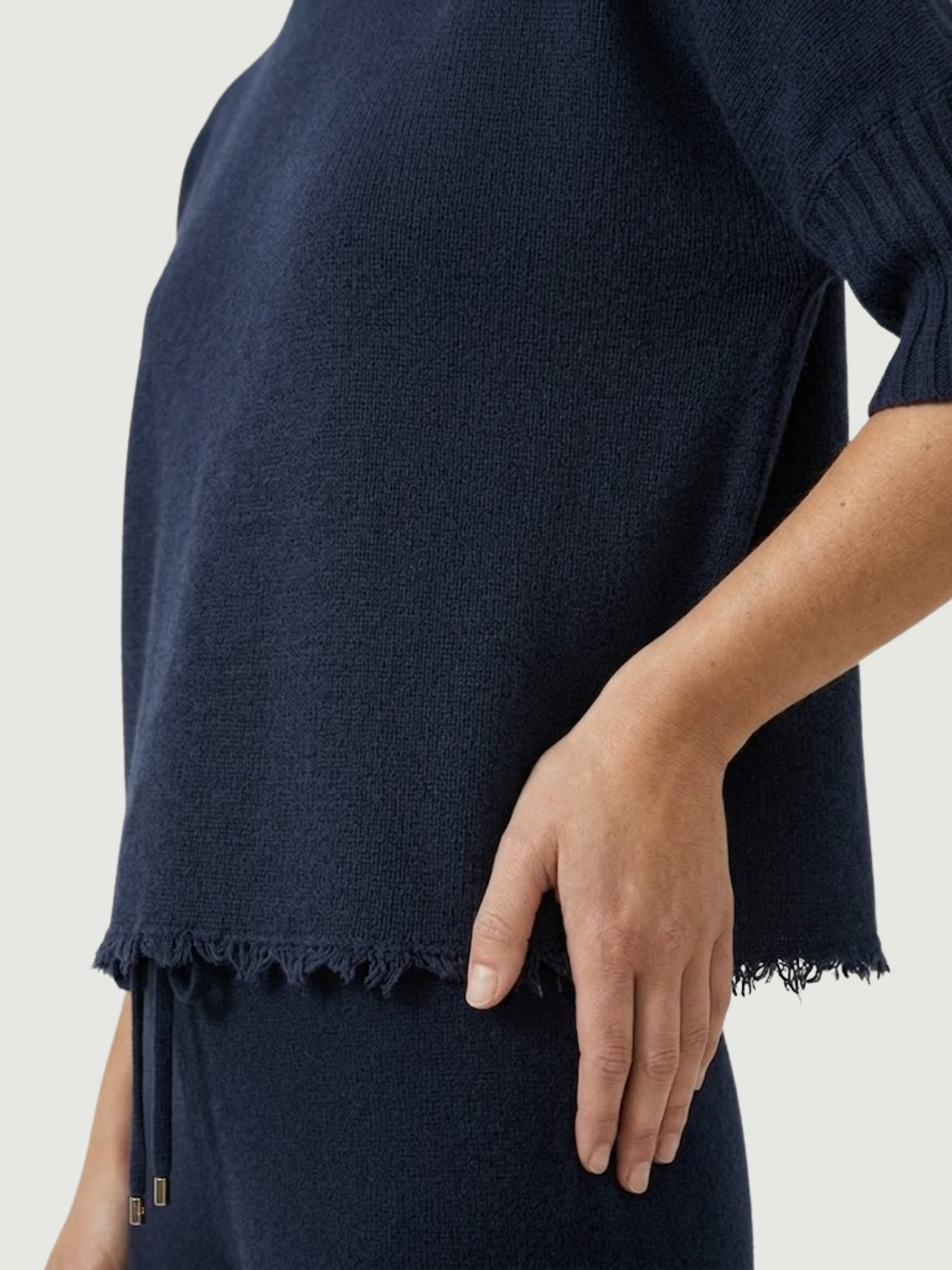 Dettaglio maglia lupetto blu scuro con manica a tre quarti e fondo sfrangiato