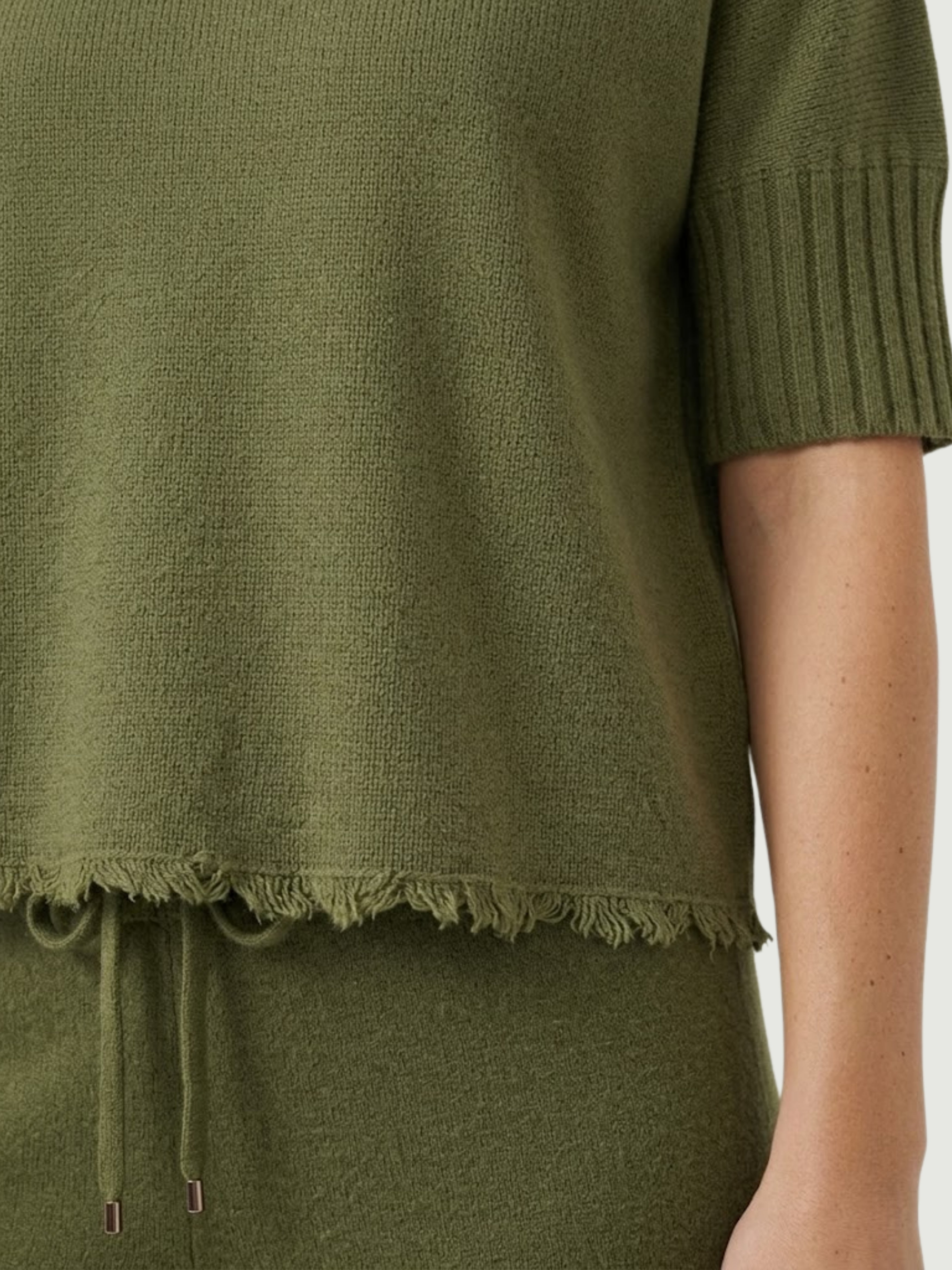 Dettaglio maglia lupetto verde oliva con manica a tre quarti e fondo sfrangiato