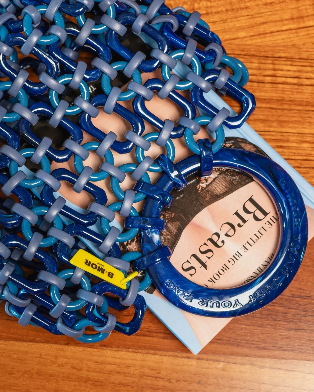 borsa a mano in resina bluette appoggiata sul tavolo con libro all'interno