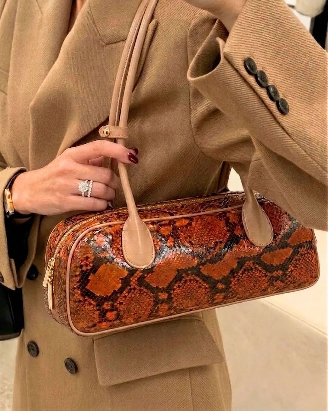 modella indossa borsa a spalla allungata in pelle di pitone arancione con manico in pelle beige