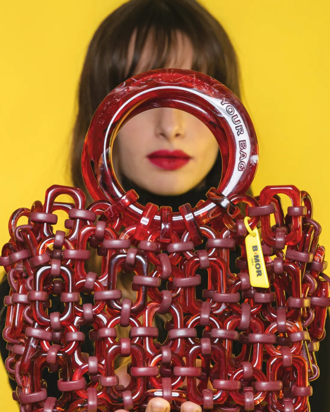 borsa a mano in resina rosso ciliegi con modella sullo sfondo