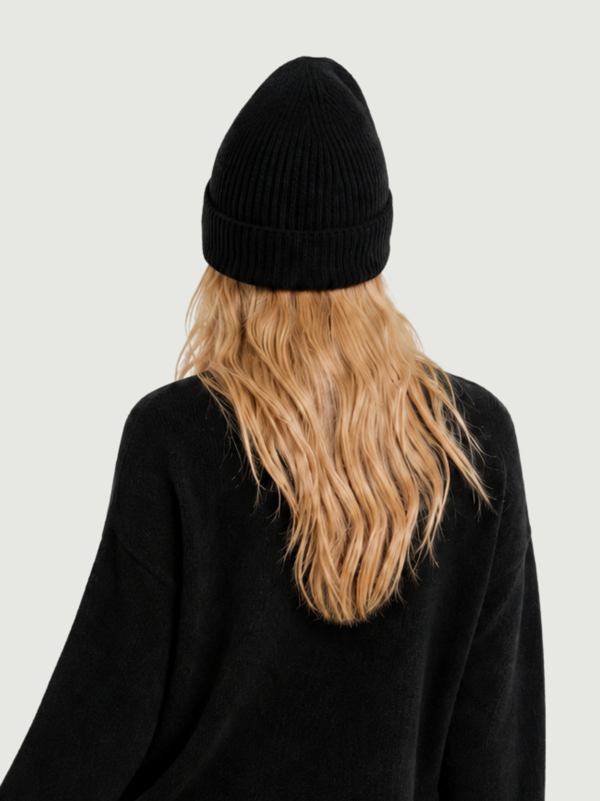Vista posteriore modella indossa berretto beanie nero a coste verticali, risvolto alto e calotta arrotondata