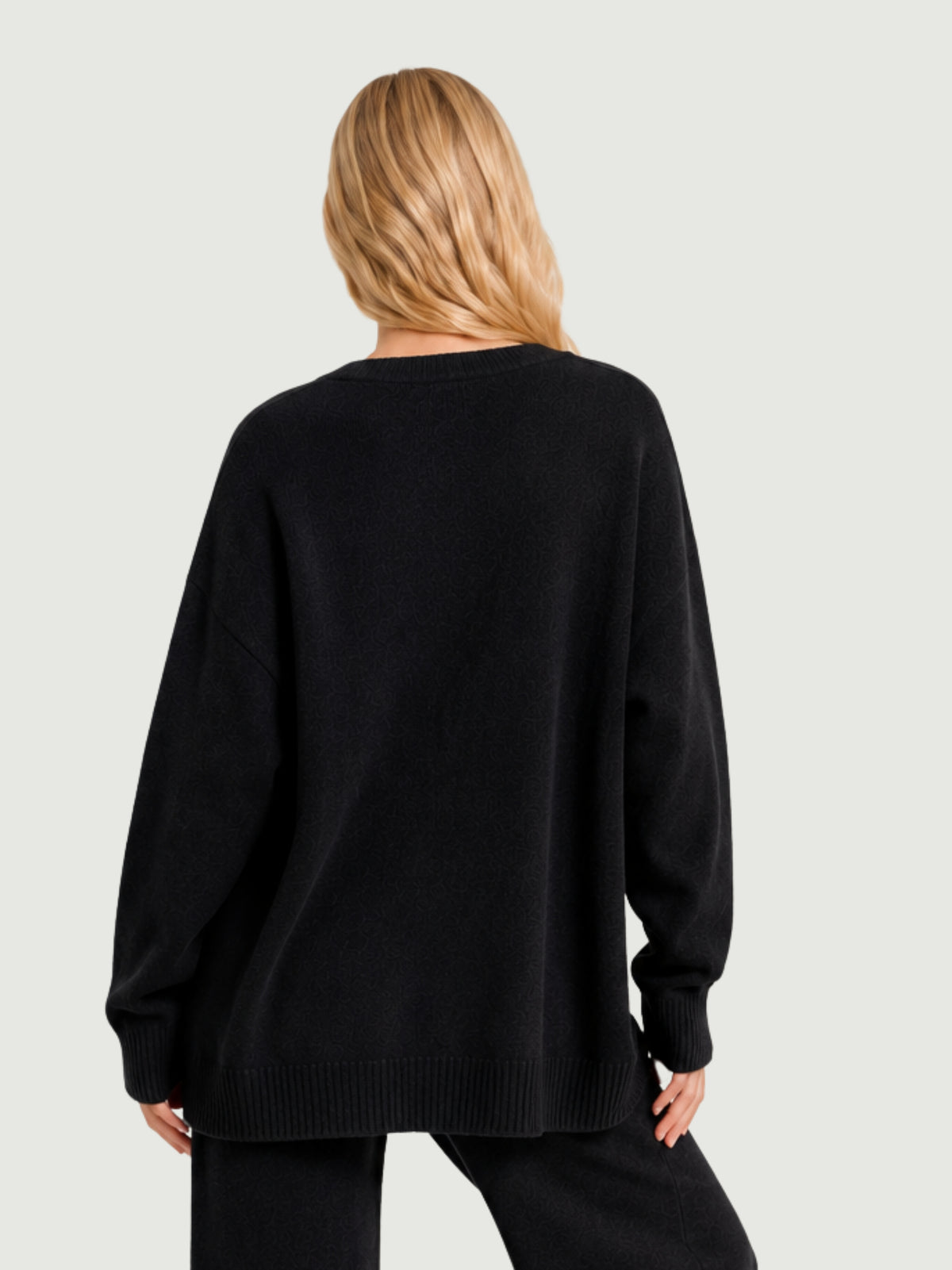 Vista posteriore modella indossa cardigan over nero, scollo a V, manica lunga con polsino a costine, chiusura con bottoni effetto madreperla