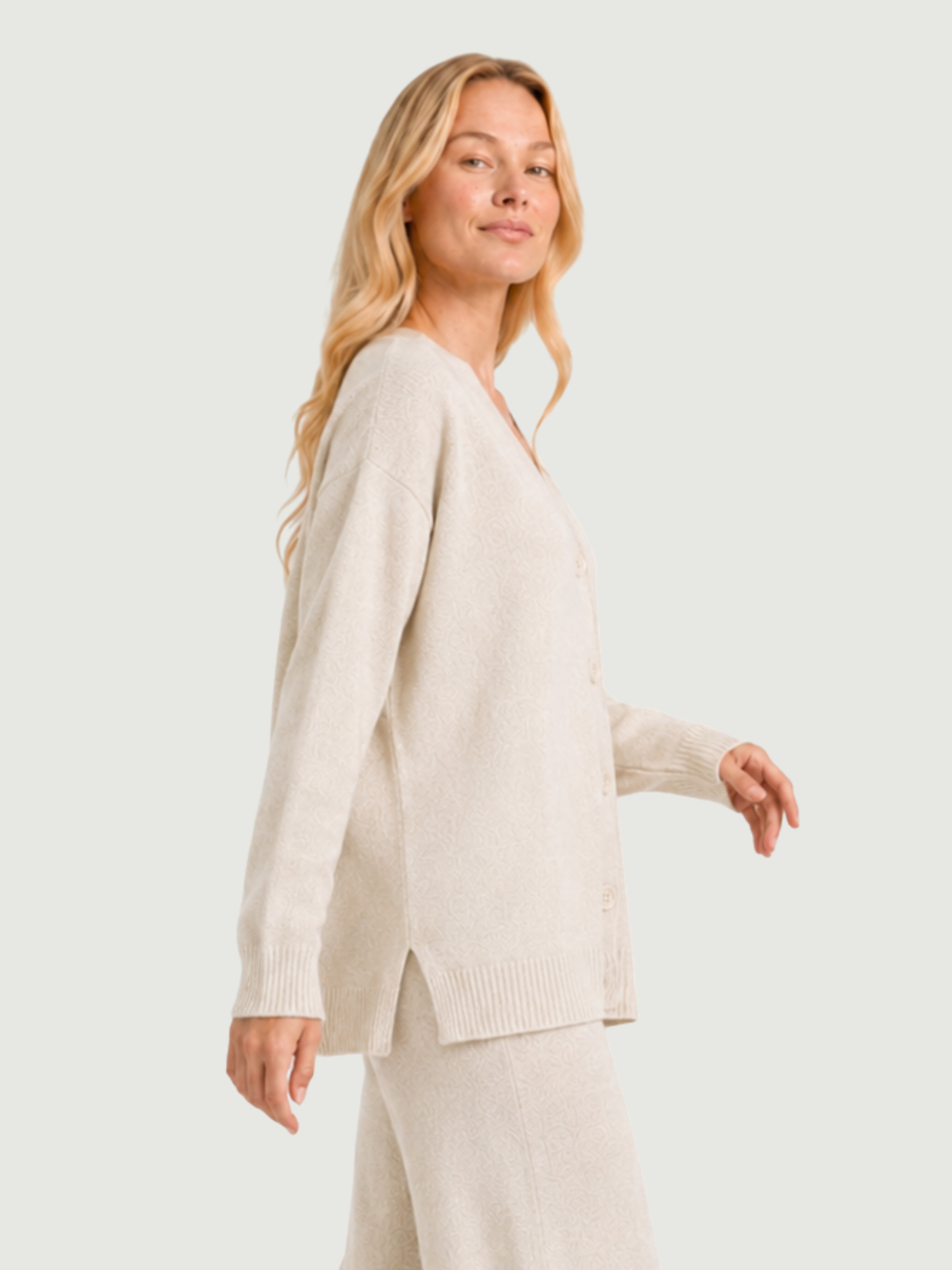 Vista laterale modella indossa cardigan over bianco panna, scollo a V, manica lunga con polsino a costine, chiusura con bottoni effetto madreperla
