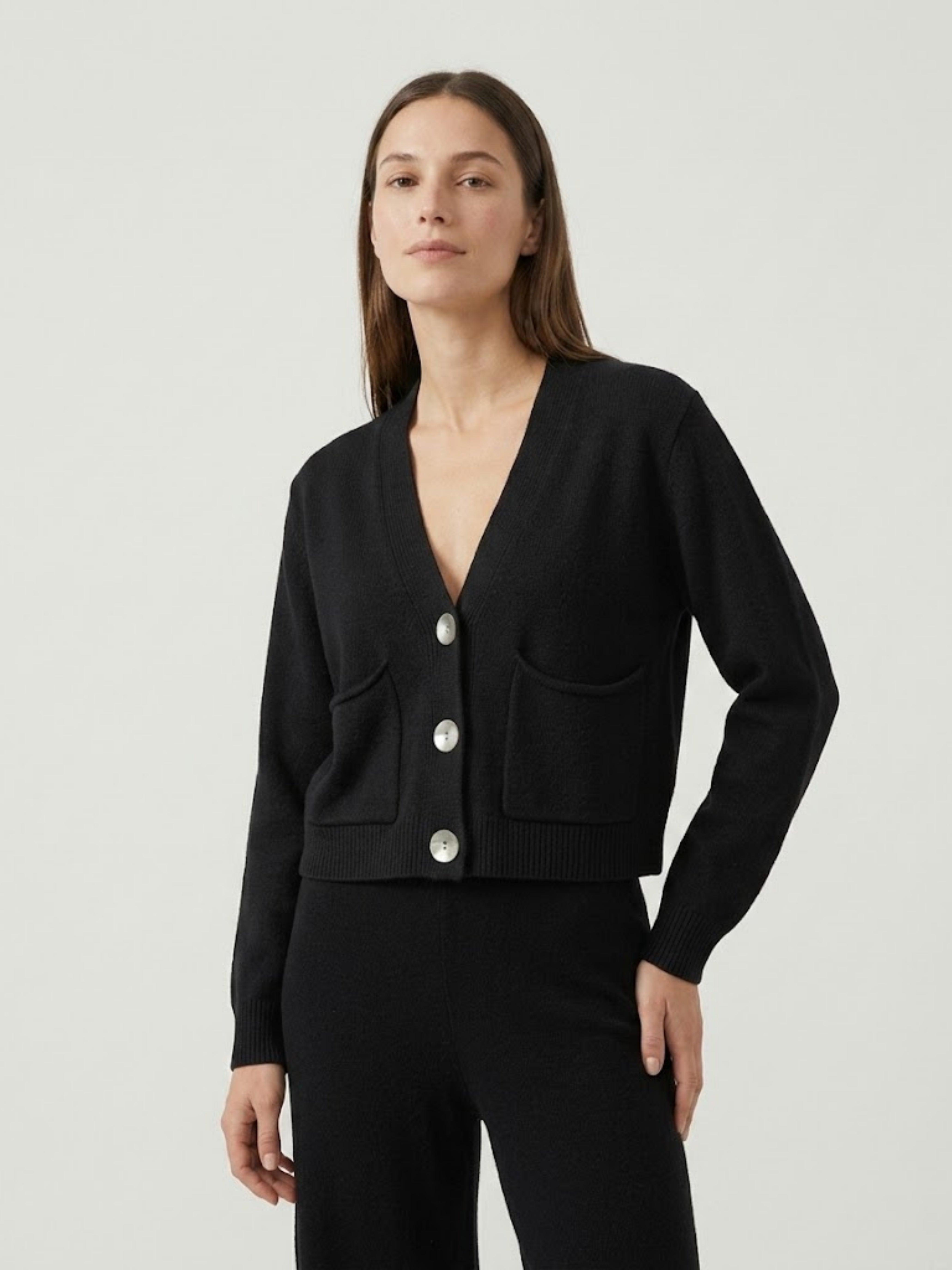 Modella indossa cardigan cropped nero con scollo a V, chiusura frontale con bottoni effetto madreperla, taschini applicati SOF - BiMOR