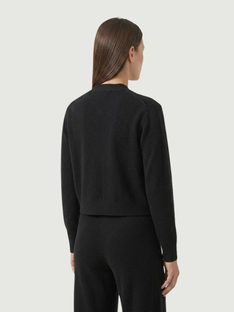 Vista posteriore modella indossa cardigan cropped nero con scollo a V, chiusura frontale con bottoni effetto madreperla, taschini applicati