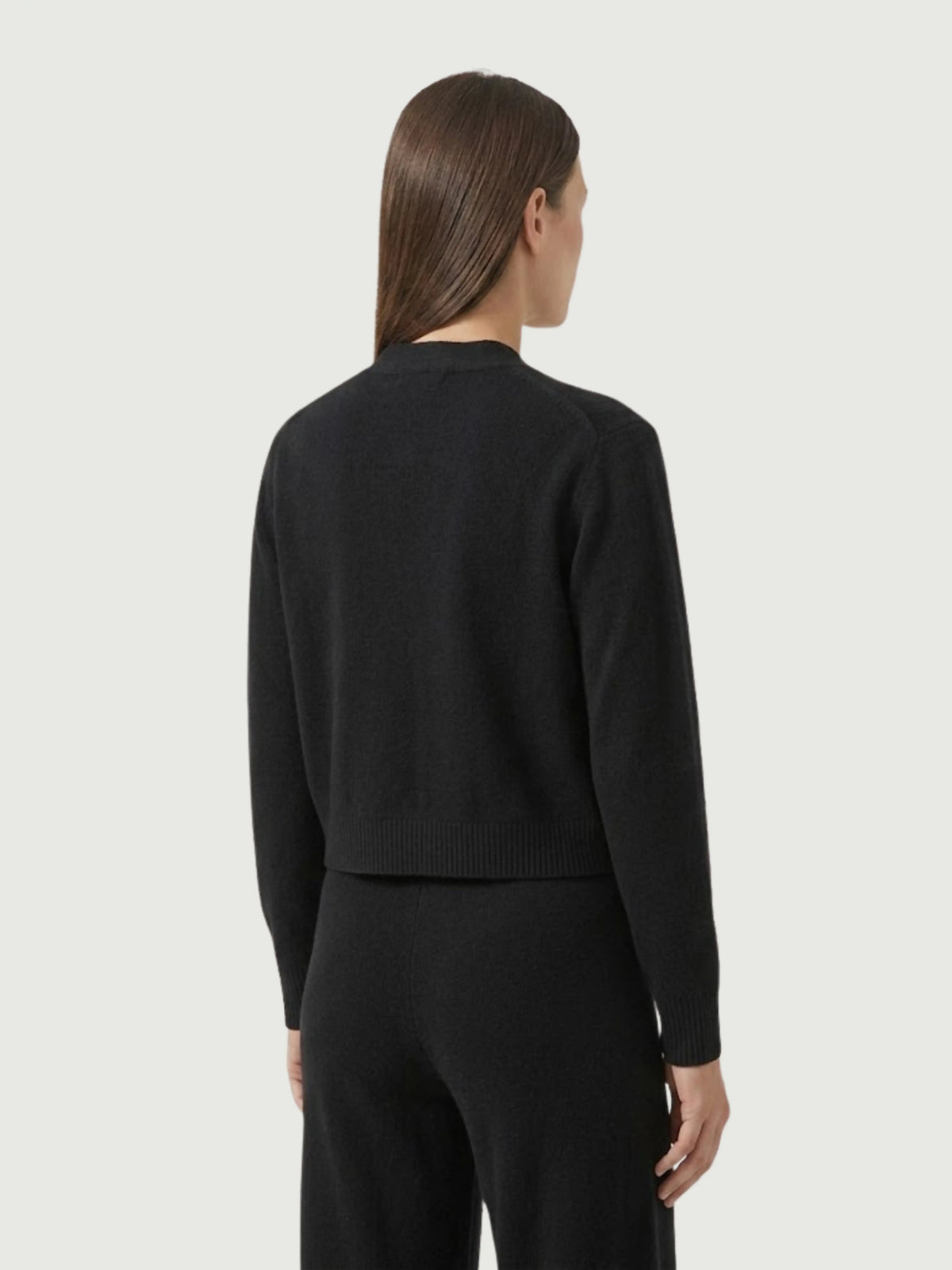 Vista posteriore modella indossa cardigan cropped nero con scollo a V, chiusura frontale con bottoni effetto madreperla, taschini applicati