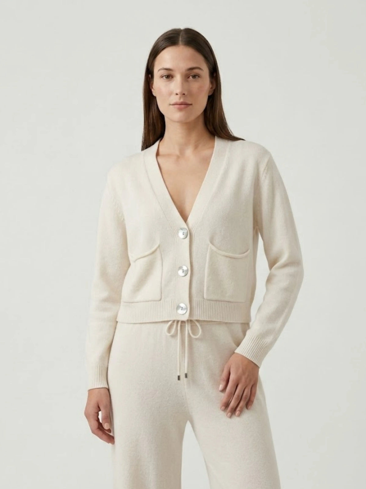 Modella indossa cardigan cropped bianco panna con scollo a V, chiusura frontale con bottoni effetto madreperla, taschini applicati SOF - BiMOR