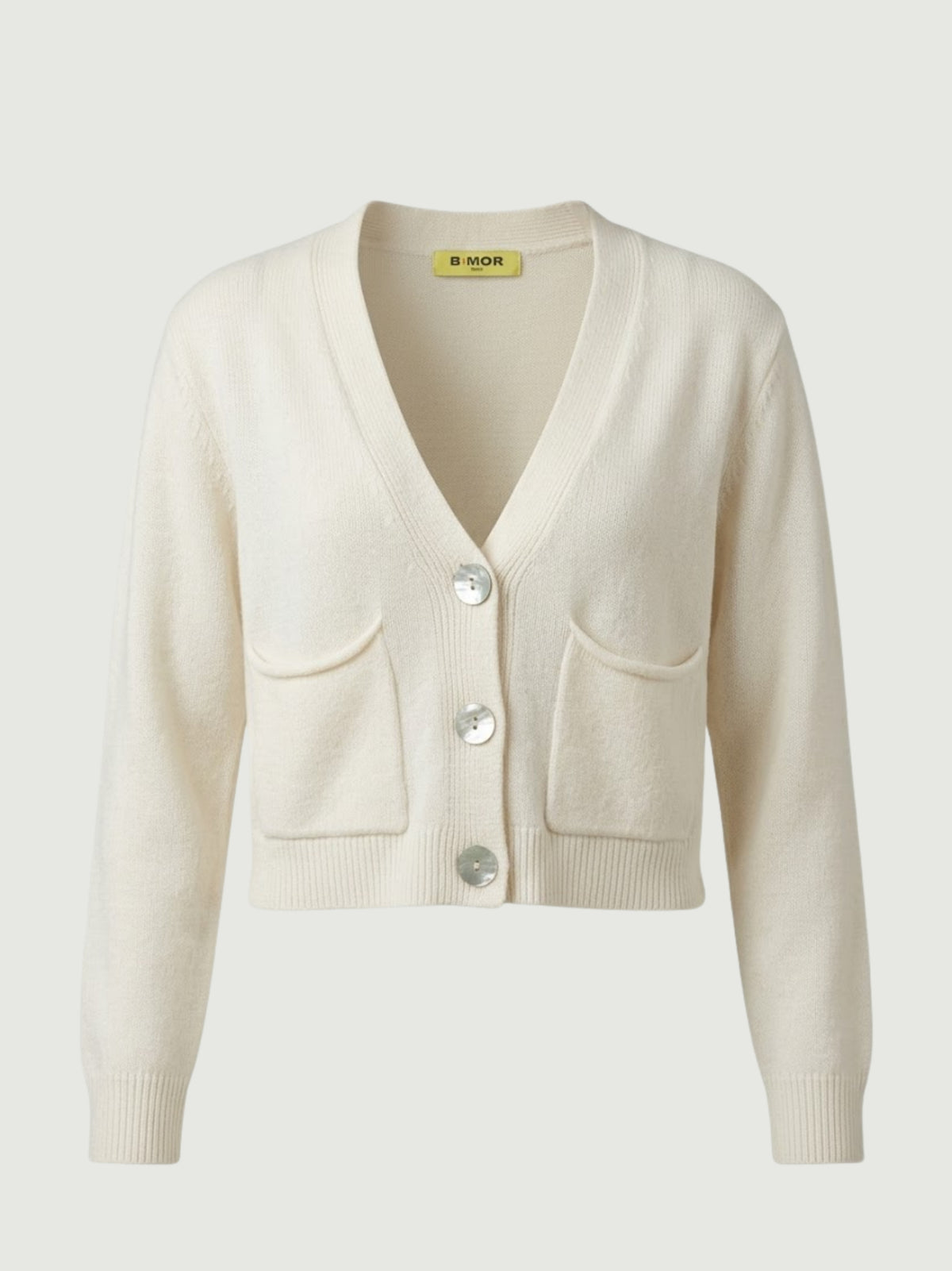 Vista frontale cardigan cropped bianco panna con scollo a V, chiusura frontale con bottoni effetto madreperla, taschini applicati