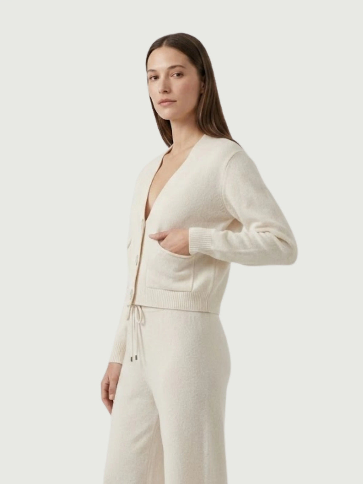 Vista laterale modella indossa cardigan cropped bianco panna con scollo a V, chiusura frontale con bottoni effetto madreperla, taschini applicati