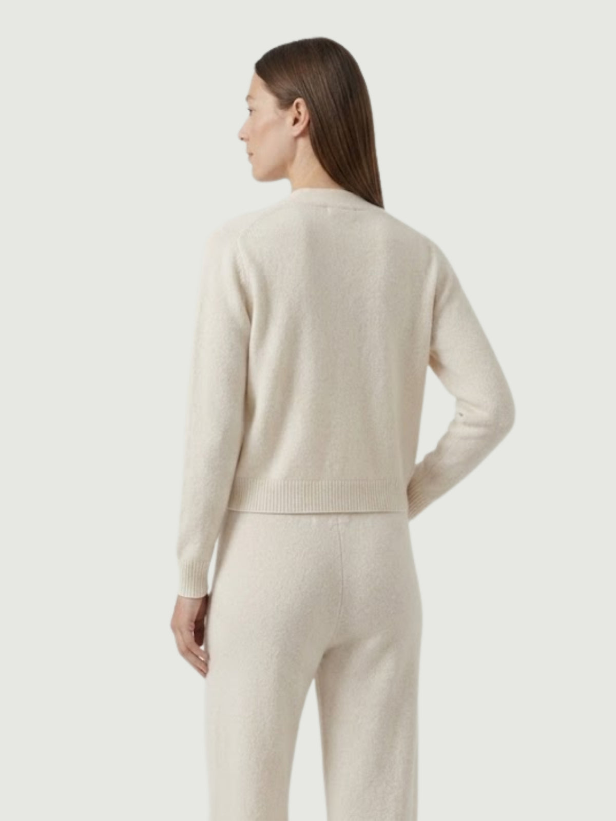 Vista posteriore modella indossa cardigan cropped bianco panna con scollo a V, chiusura frontale con bottoni effetto madreperla, taschini applicati