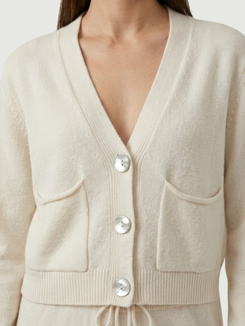 Dettaglio cardigan cropped bianco panna con scollo a V, chiusura frontale con bottoni effetto madreperla, taschini applicati