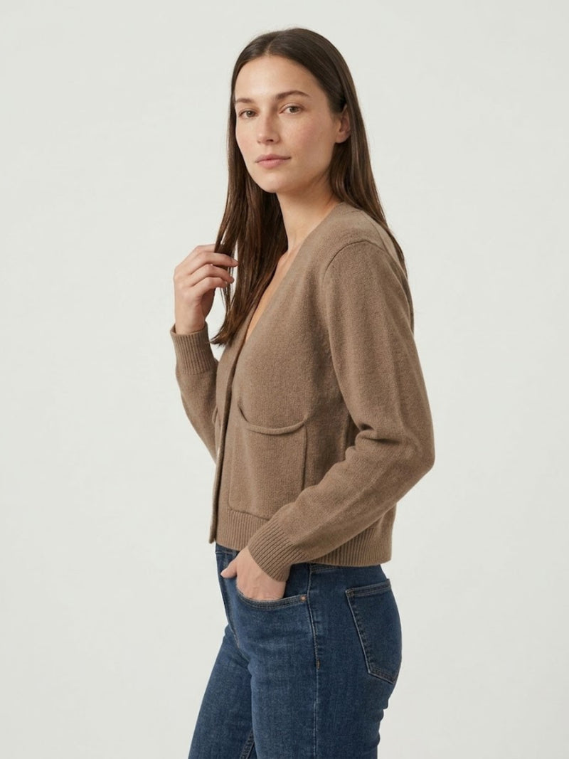 Vista laterale modella indossa cardigan cropped nocciola con scollo a V, chiusura frontale con bottoni effetto madreperla, taschini applicati