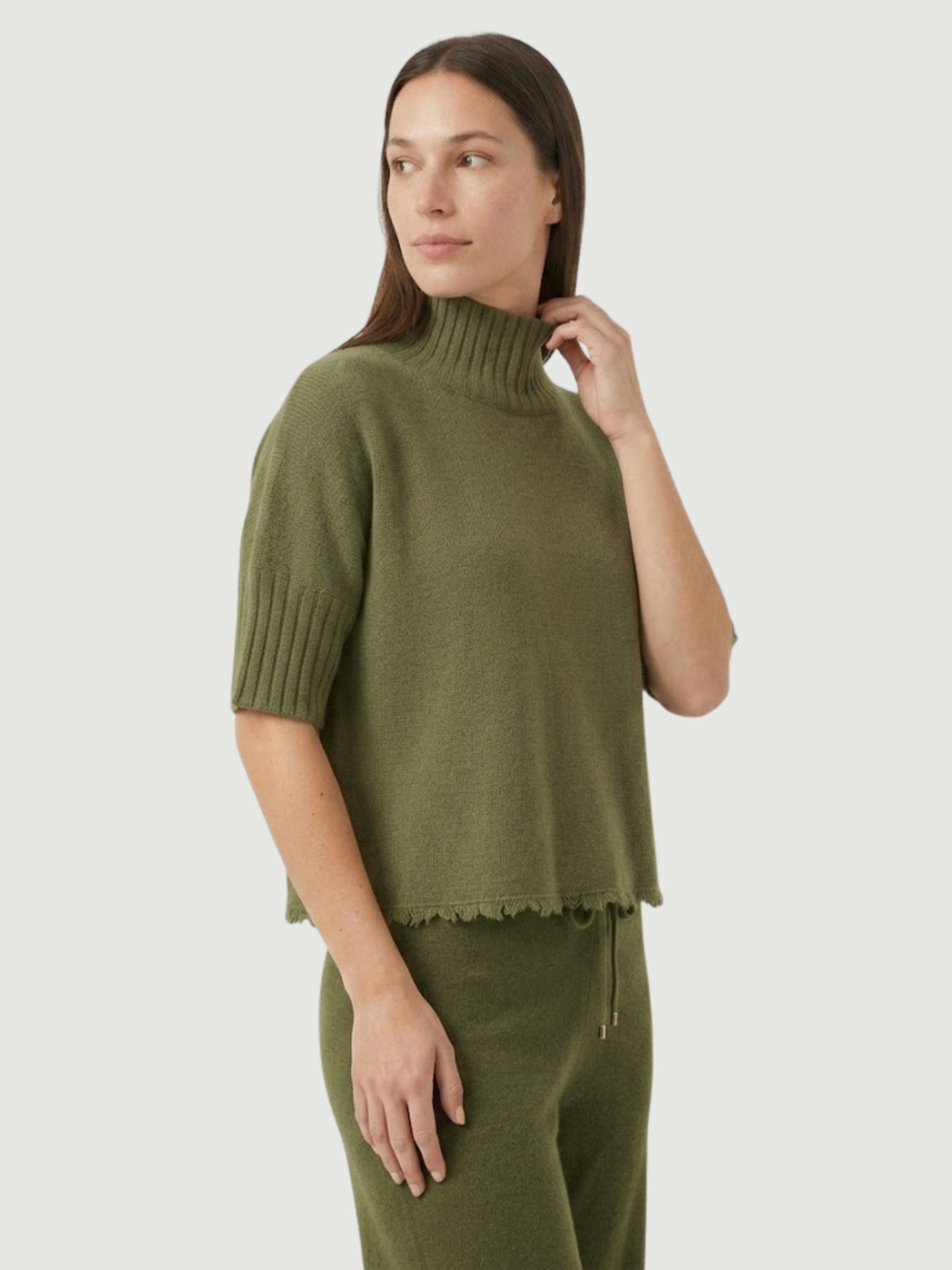 Vista laterale modella indossa maglia lupetto verde oliva con manica a tre quarti e fondo sfrangiato