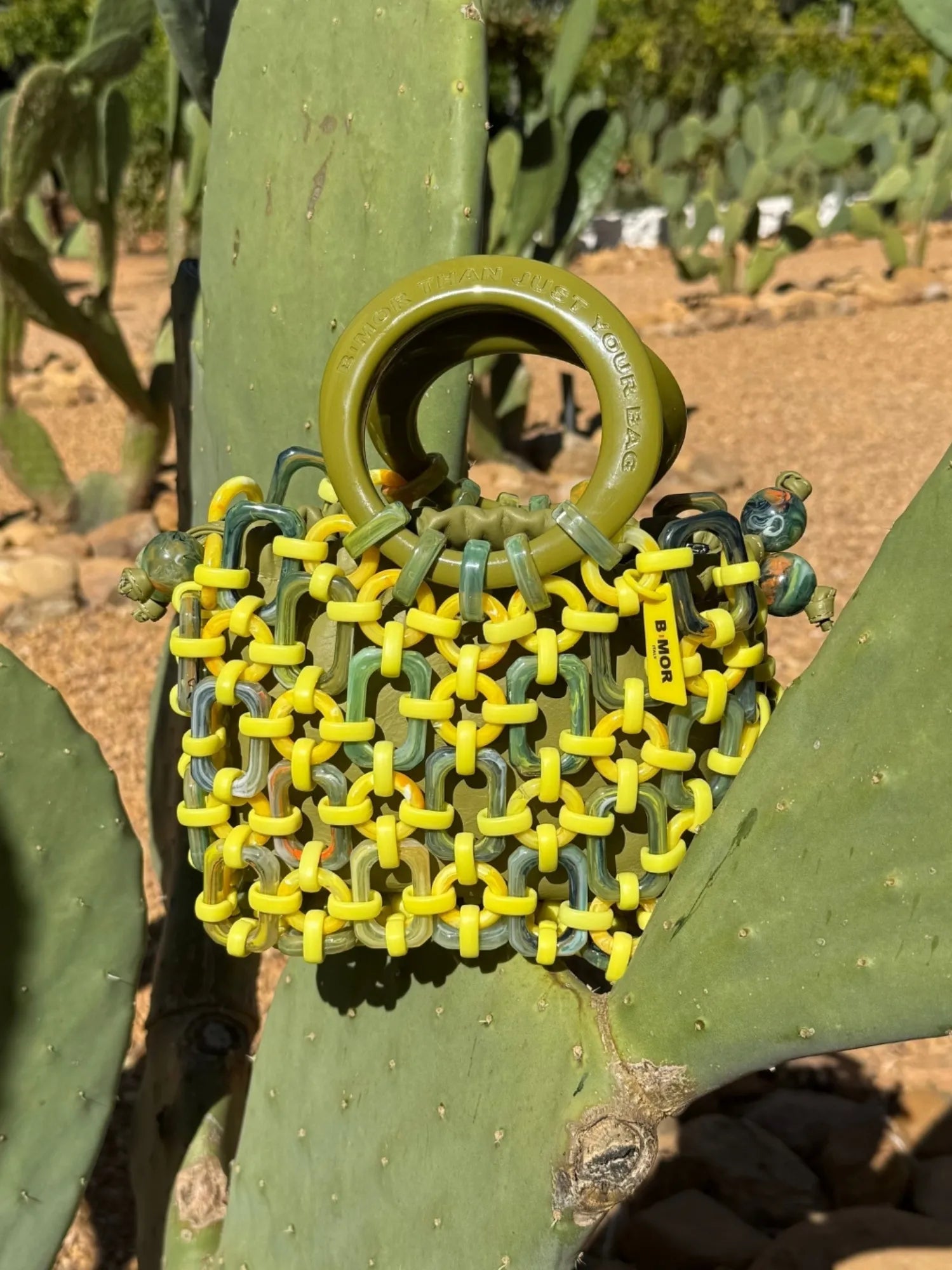 borsa a mano in resina verde e gialla appoggiata su cactus