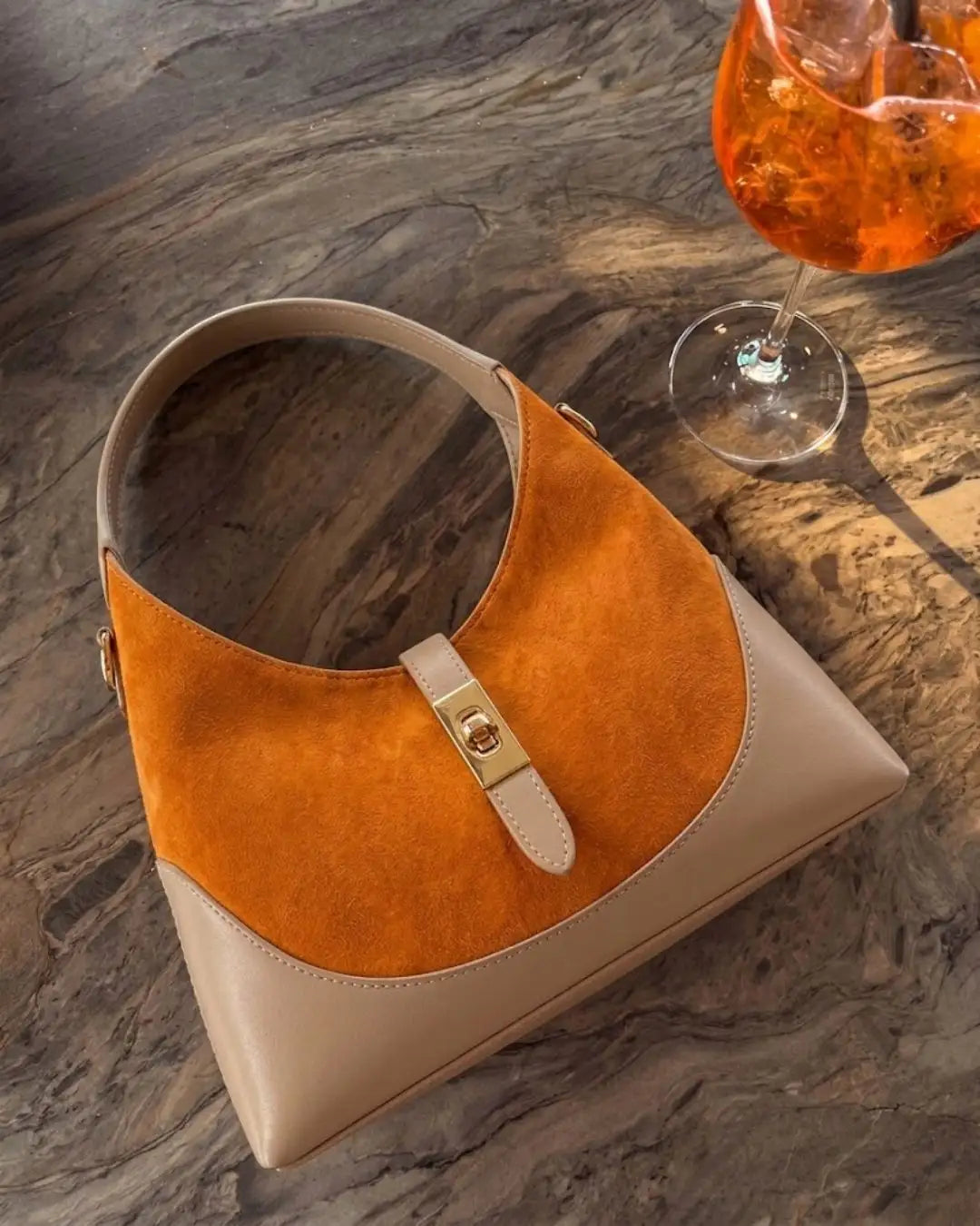 borsa a spalla elegante in pelle di camoscio arancione con manico e dettagli in pelle beige appoggiata